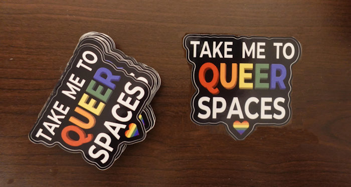 TAKE ME TO QUEER SPACES sticker displayed in a business